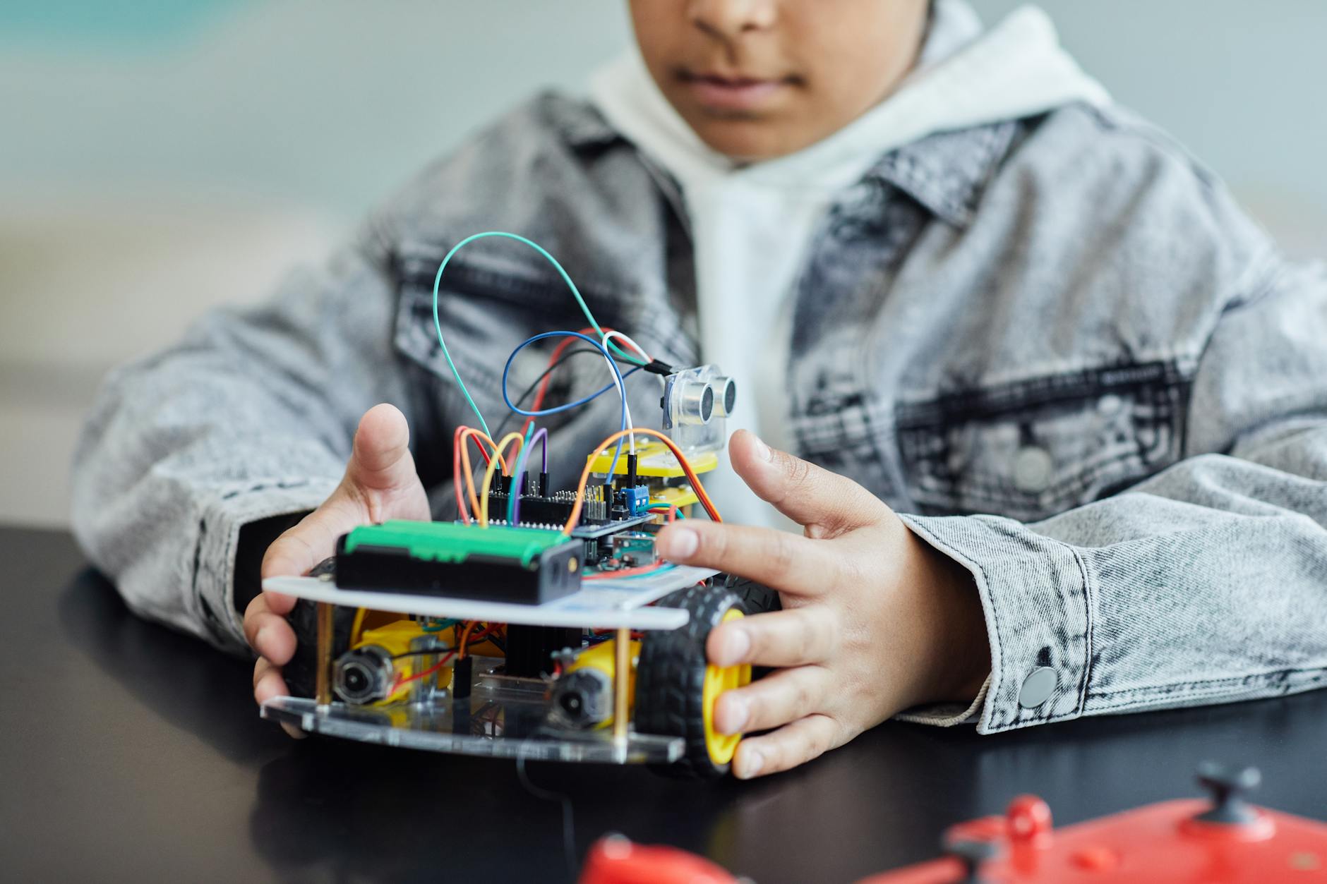 boy in denim jacket holding a toy with electric wires and wheel