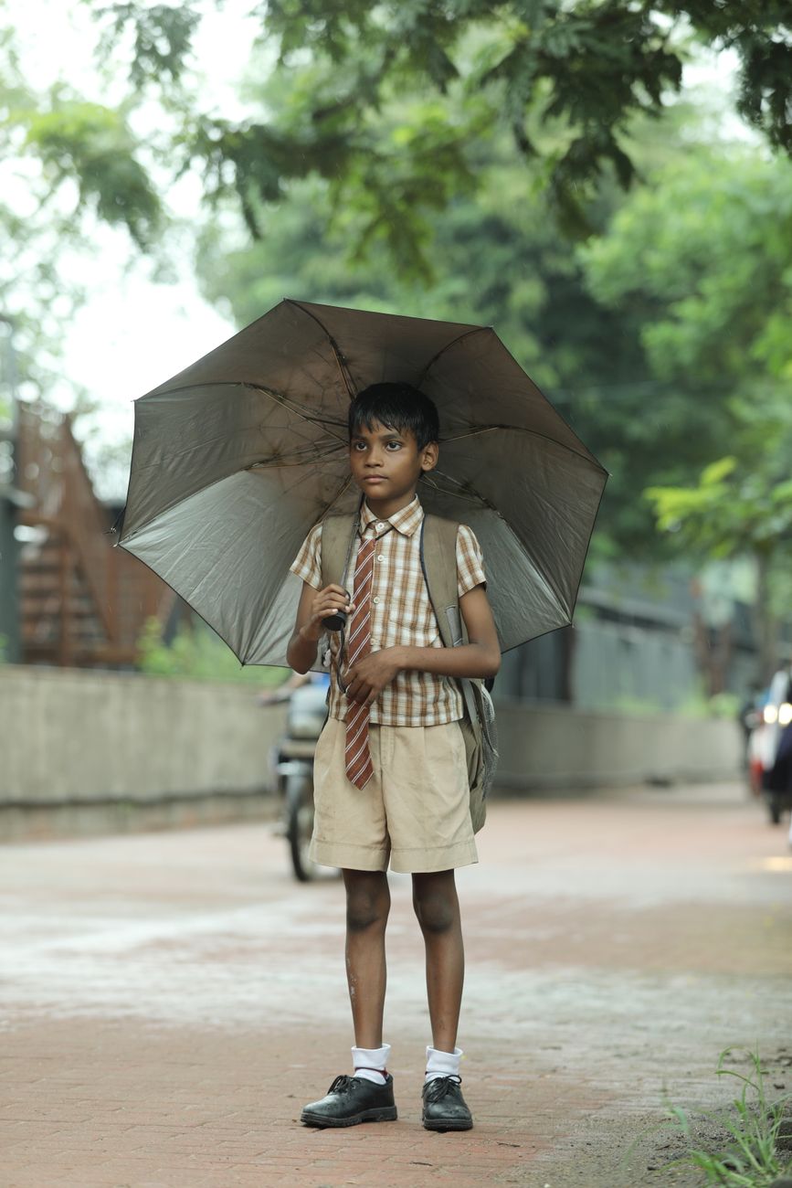 young indian boy holding umbrella on rainy day